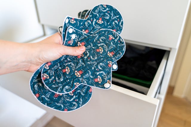 Hand holding reusable cloth menstrual pads near open cabinet drawer.