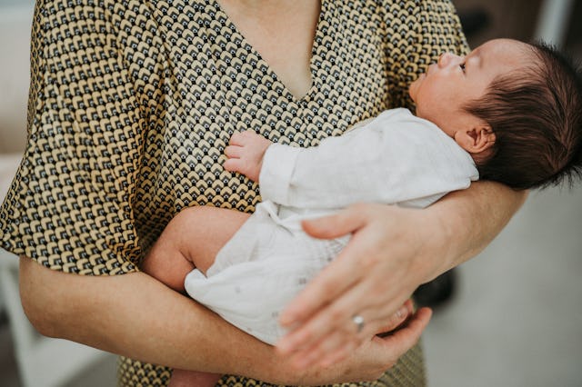 A close-up of a person holding a baby, wrapped in a white outfit. The adult’s hand gently supports t...