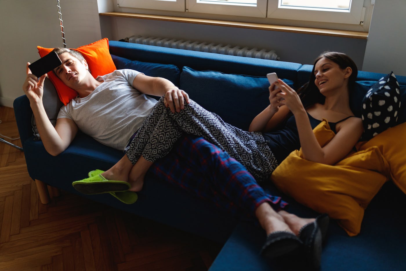 Lazy morning for a young couple using mobile phones on the sofa still in pajamas