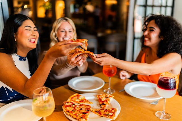 Friends women talking and eating pizza at restaurant