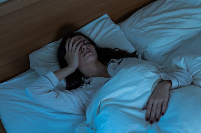 Sleepless young woman suffering from insomnia, covering eyes with hands