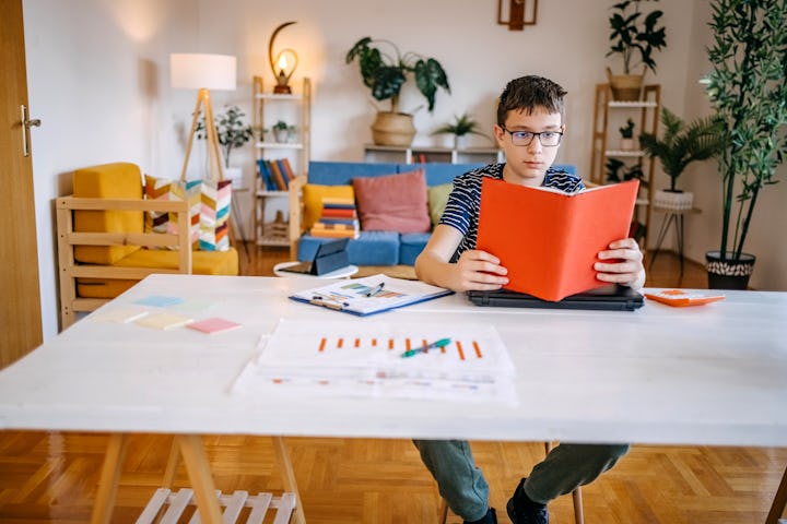 Teenager holding book in hand and trying to study while sitting in living room