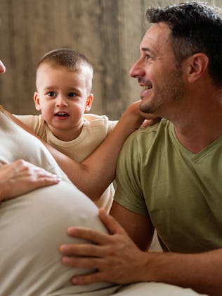 A joyful family moment with a pregnant woman, her smiling partner, and their playful young son, all ...