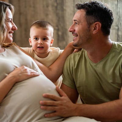 A joyful family moment with a pregnant woman, her smiling partner, and their playful young son, all sharing a tender interaction indoors.
