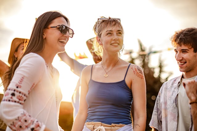 A lively group of young adults celebrates together at a music festival, dancing and laughing under t...