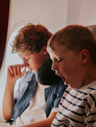 Two young lads wait patiently on a flight to their vacation destination. The younger brother yawns.