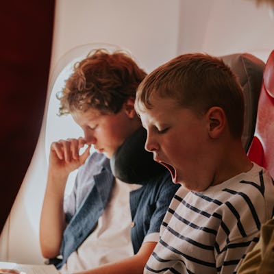 Two young lads wait patiently on a flight to their vacation destination. The younger brother yawns.