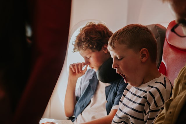 Two young lads wait patiently on a flight to their vacation destination. The younger brother yawns.