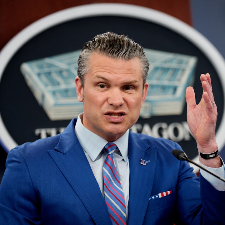 Secretary of Defense Pete Hegseth in a blue suit gestures while speaking at a podium, with a Pentago...