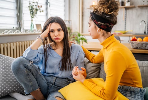 Young woman comforting her sad friend by holding her hand and engaging in heartfelt conversation in ...