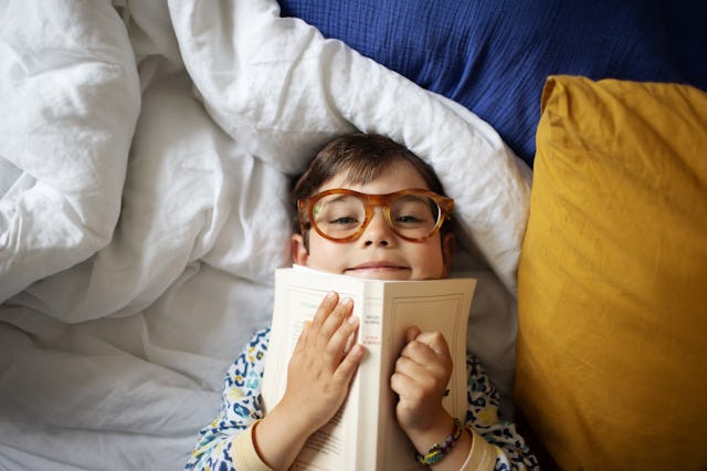 Portrait of a smiling little boy at home, he's wearing adult's glasses and pretending to read his pa...