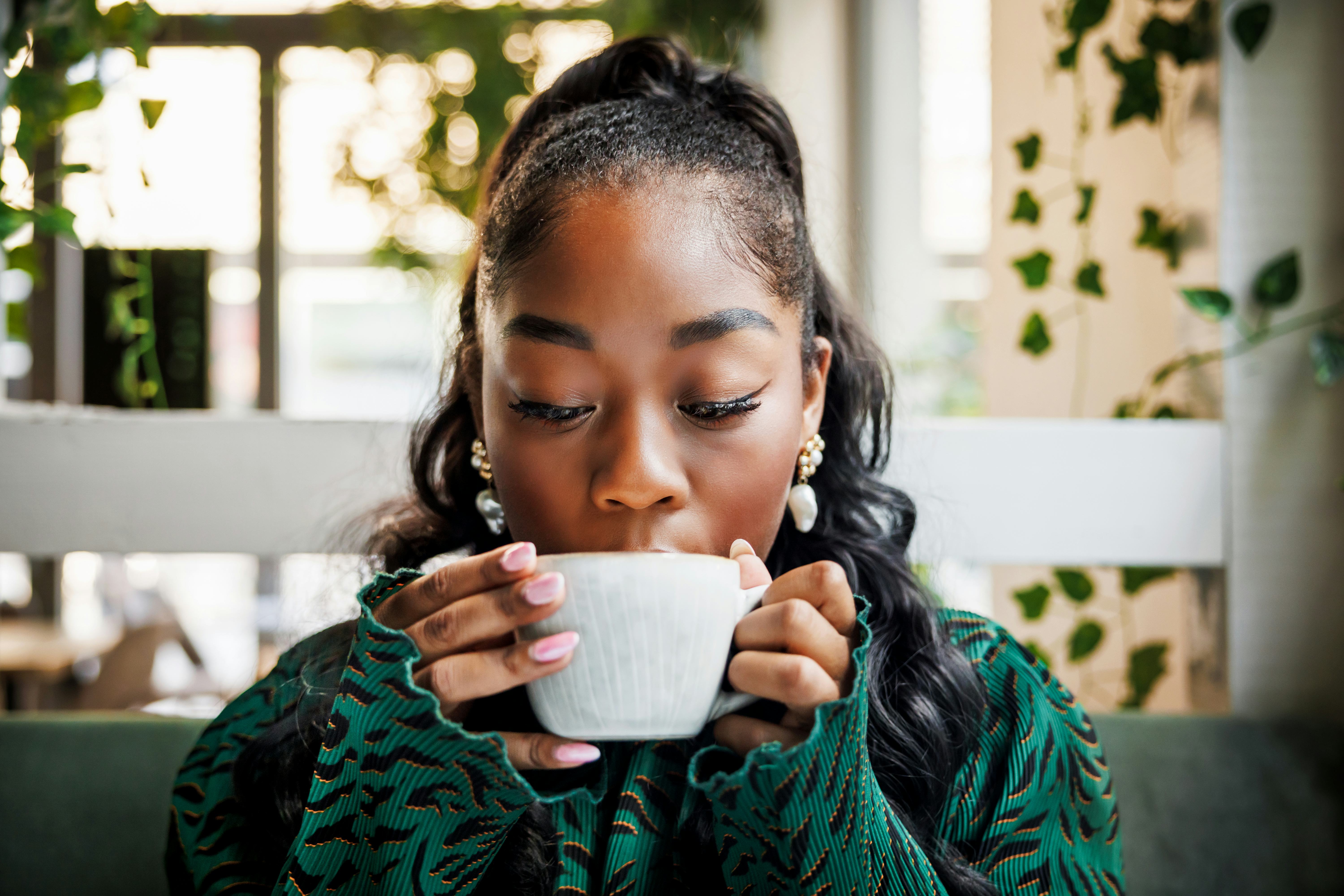 A young woman indulges in the aroma of her coffee, closing her eyes to savor the moment in a leafy c...