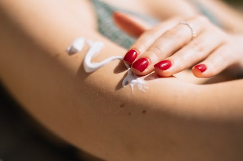 Close-up view of an unrecognisable woman applying suntan cream to her skin while sunbathing