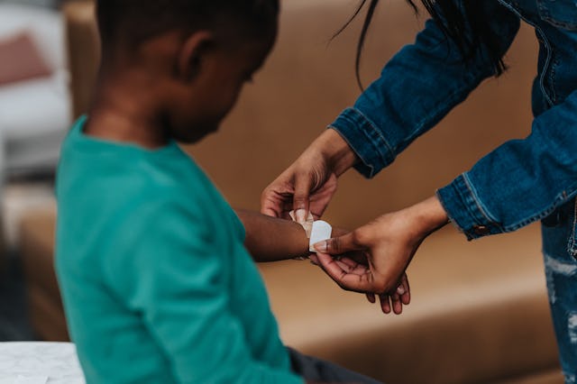 Cropped view of a preschool age black boy holding out his hurt wrist so his mom can place an adhesiv...