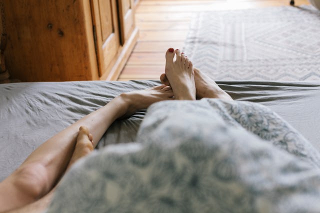 First person perspective of young couple's feet while lying in Bed.