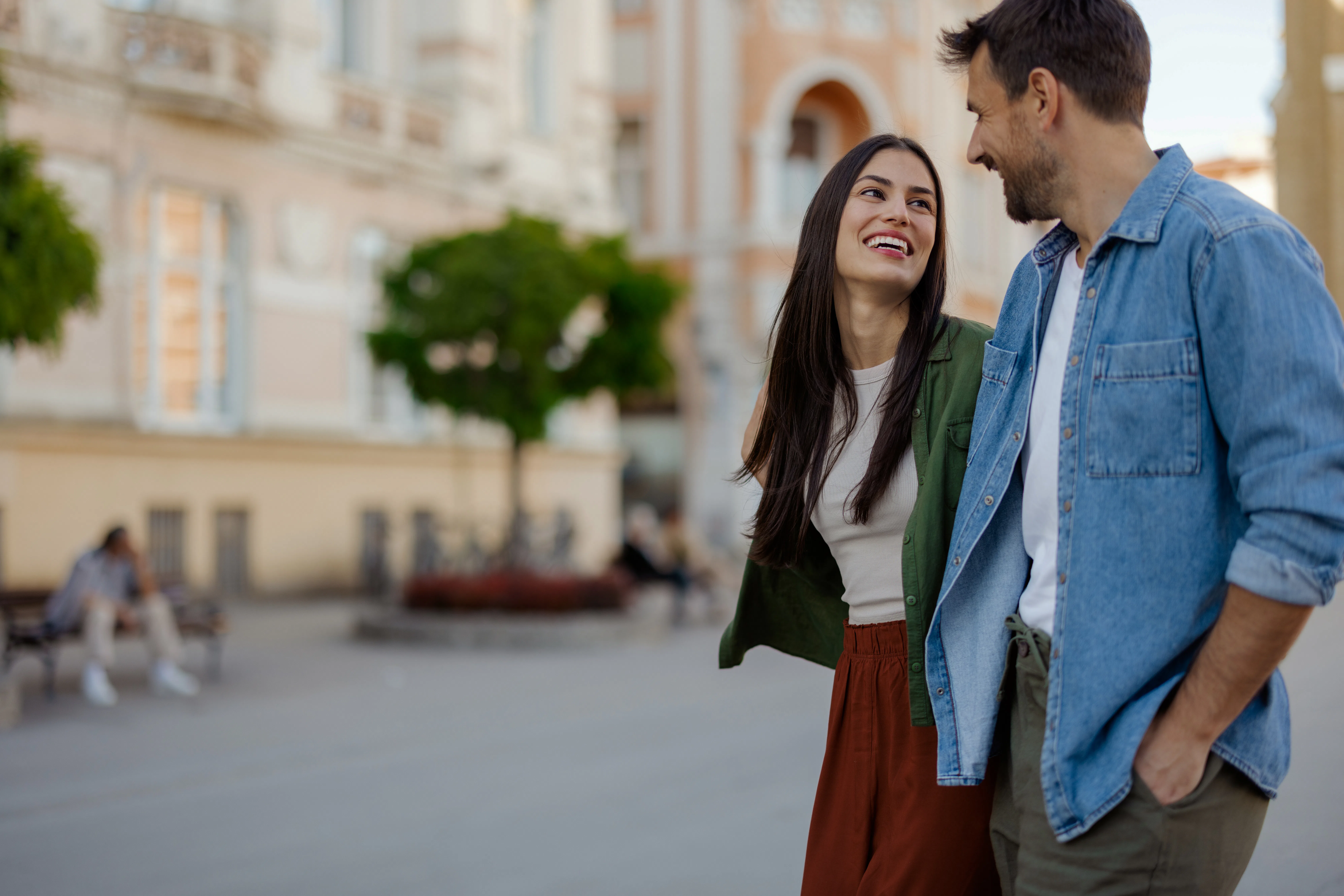 Happy couple in casual stylish outfits walking through an urban street, sharing smiles and creating ...