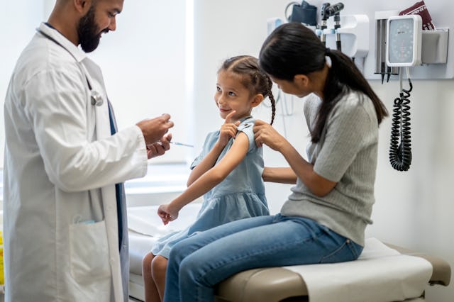 A young girl around 7 years old is at a doctor's office with her mother. They are both sitting on an...