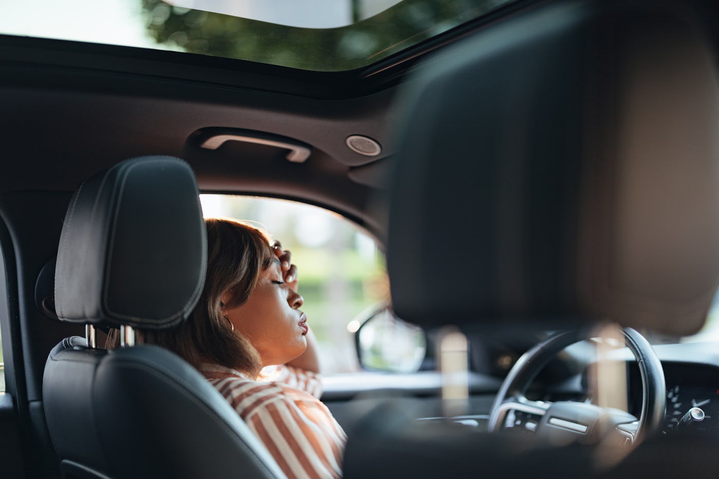 A focused African American businesswoman is seen driving a car in a city setting, capturing a moment of concentration and urban commute.