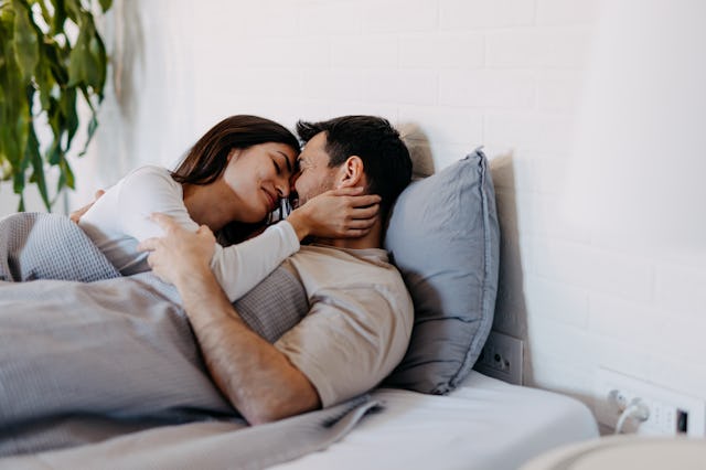 Happy young couple cuddling in bed, sharing love and affection as morning light fills the cozy bedro...