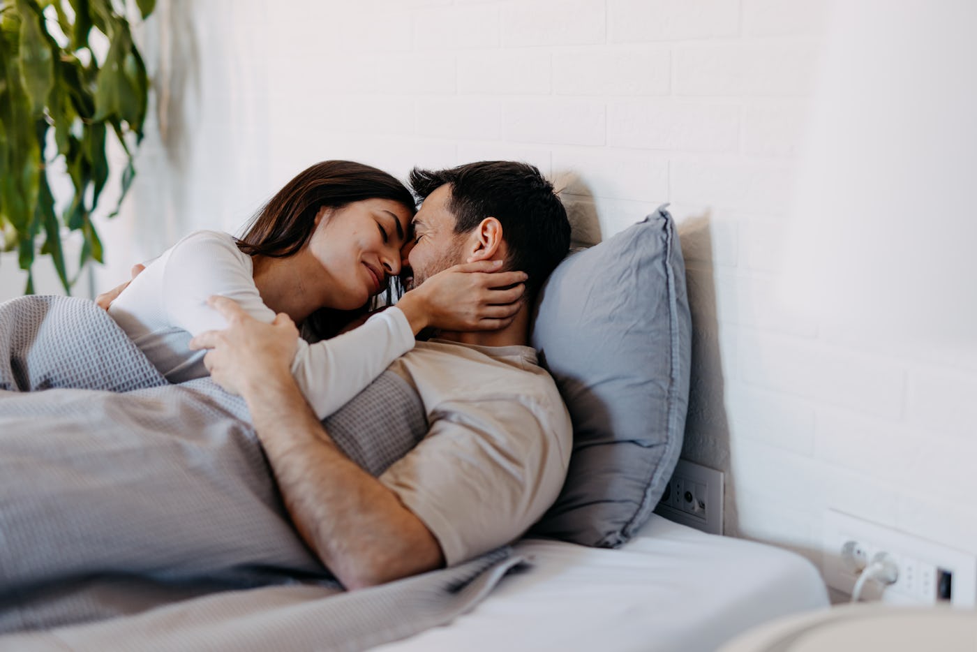 Happy young couple cuddling in bed, sharing love and affection as morning light fills the cozy bedroom. Embracing each other, they enjoy a tender moment of intimacy and connection