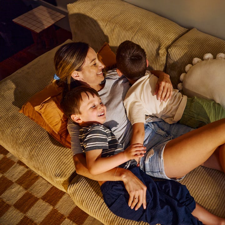 Mother having fun with her two sons, laughing and playing on the sofa in the living room at home