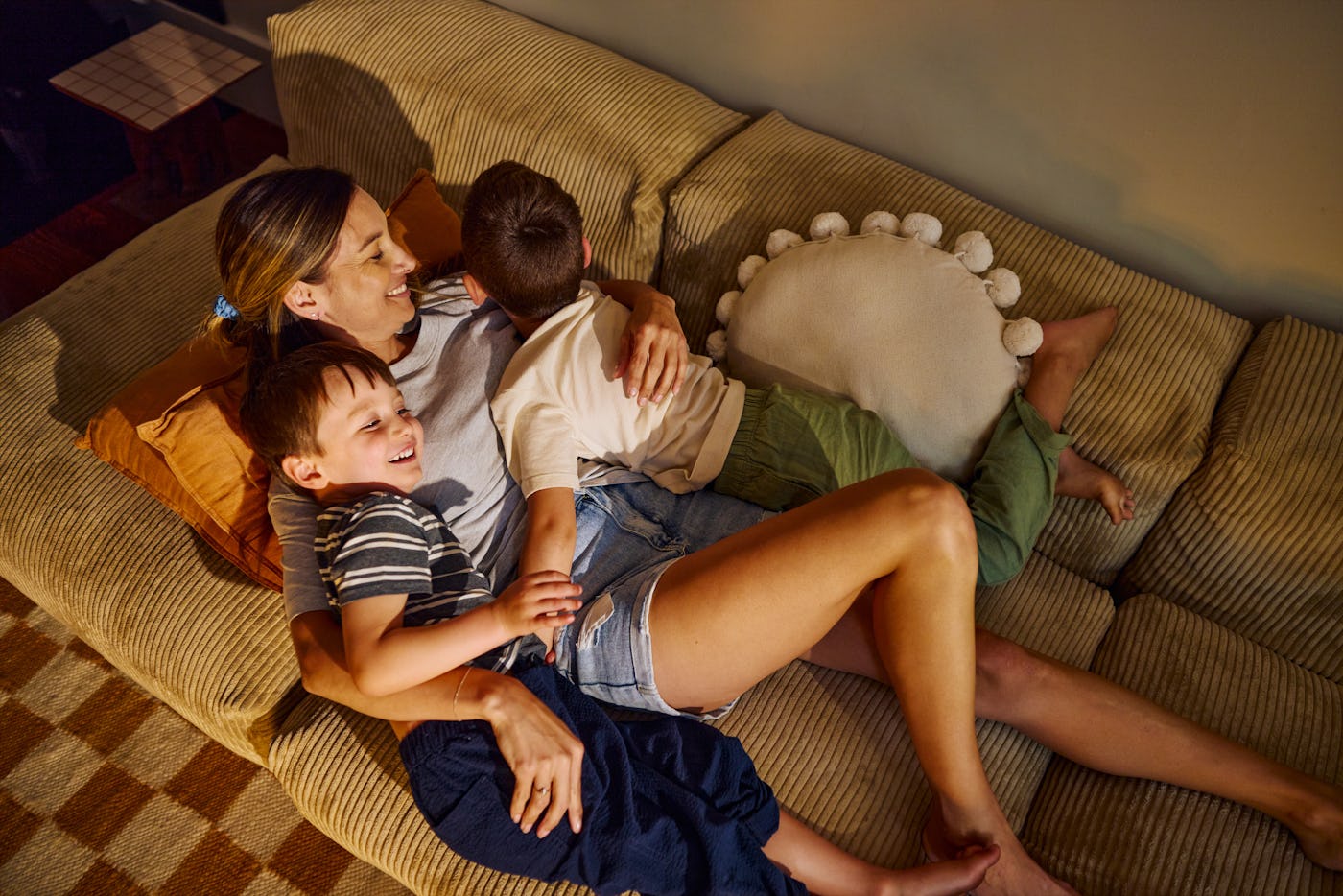 Mother having fun with her two sons, laughing and playing on the sofa in the living room at home
