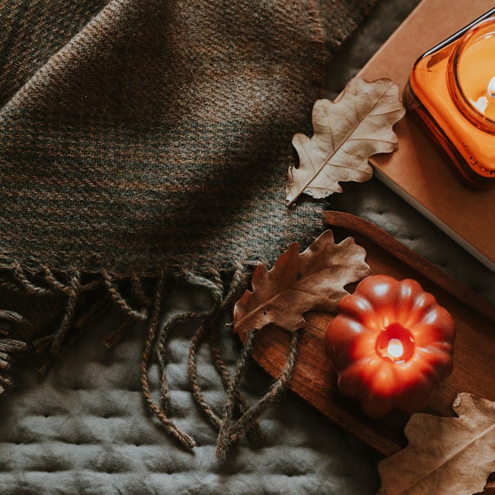 Atmospheric burning candle shape of pumpkin and candle in amber glass jar, cozy plaid, autumn leaves...