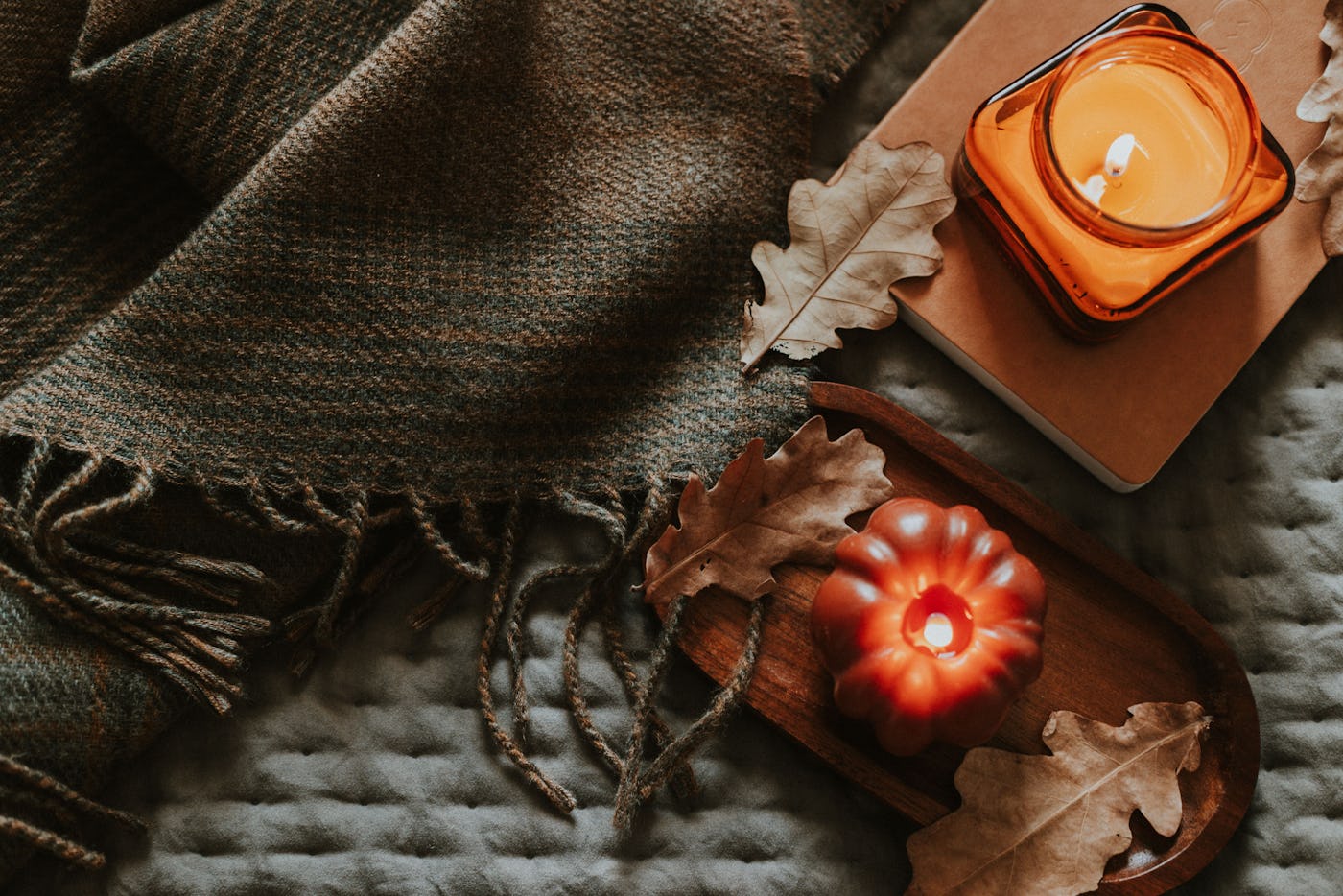 Atmospheric burning candle shape of pumpkin and candle in amber glass jar, cozy plaid, autumn leaves. Cozy autumn lifestyle, hygge concept. Still life