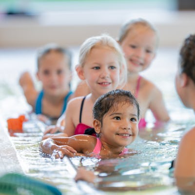 A group of children learning to swim with an instructor, smiling and enjoying the lesson in a swimming pool, promoting water skills and fun.