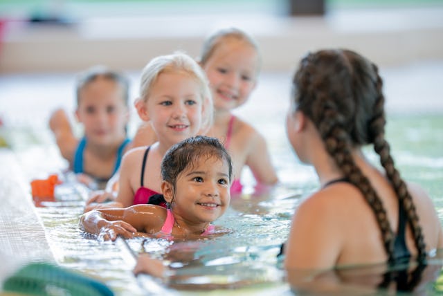 A group of children learning to swim with an instructor, smiling and enjoying the lesson in a swimmi...