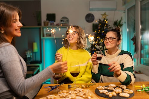 Three young female friends holding sparklers while enjoying gingerbread cookies and glass of red win...