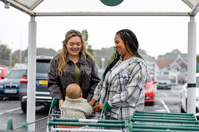 Woman, her baby who is sitting in a shopping trolley and a friend ready to go into a supermarket. Sh...