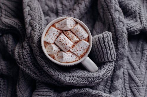 Mug of hot cacao with marshmallow on warm cozy gray sweater. Directly above. Cozy and hygge concept