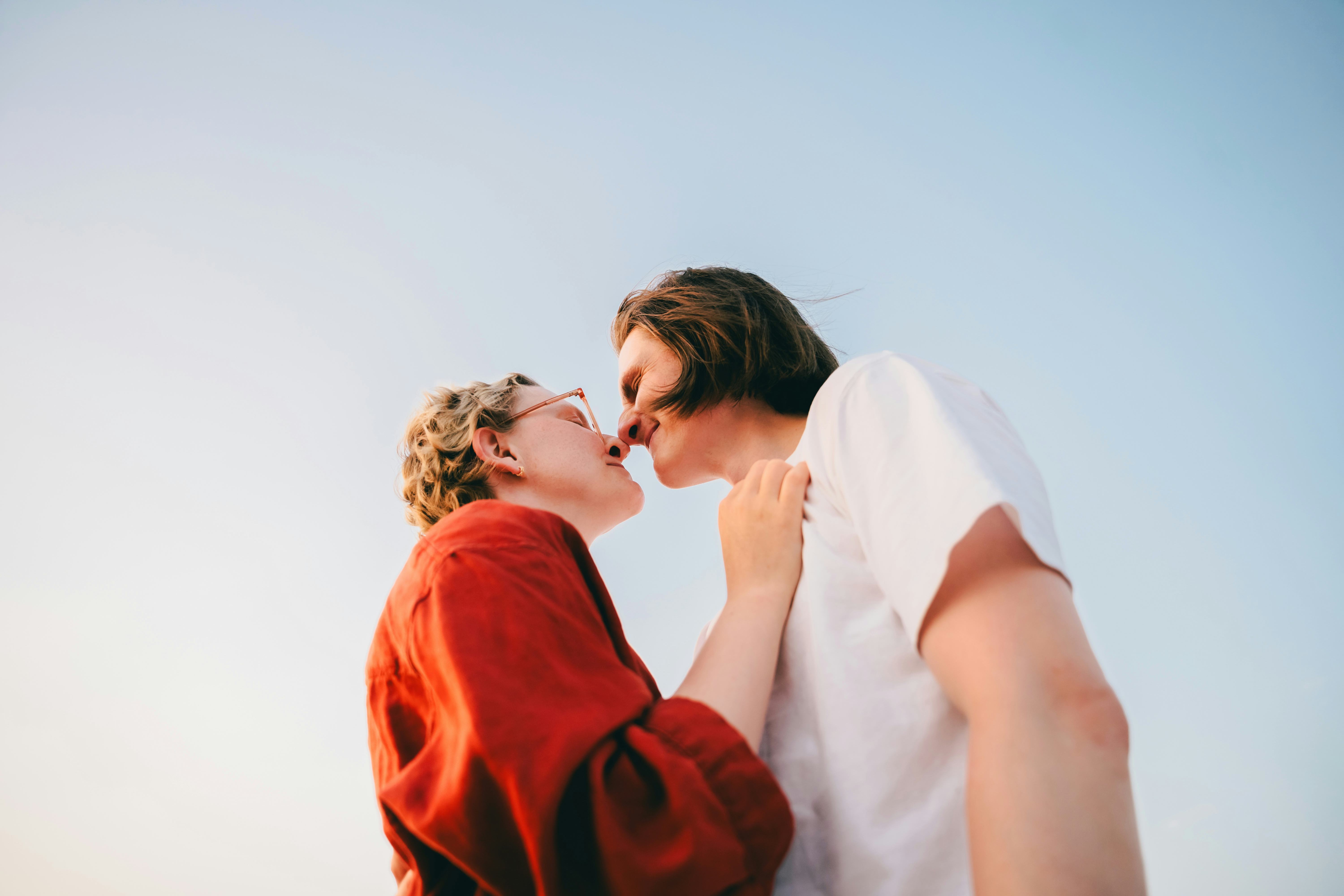 A candid photo of two individuals sharing a close and affectionate moment outdoors, with a bright an...