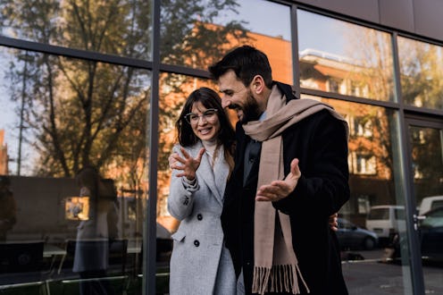 A handsome young man and his girlfriend walk arm in arm, smiling brightly and laughing as they enjoy...