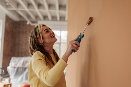 Young woman engaged in home improvement project, refreshing living room walls with rollers and paint...
