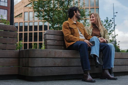 Young couple holding hands and talking while sitting on a bench in an urban environment, enjoying a ...