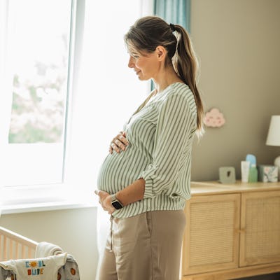 Pregnant woman standing next to crib and smiling.