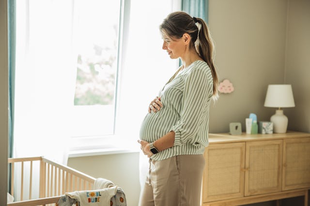 Pregnant woman standing next to crib and smiling.