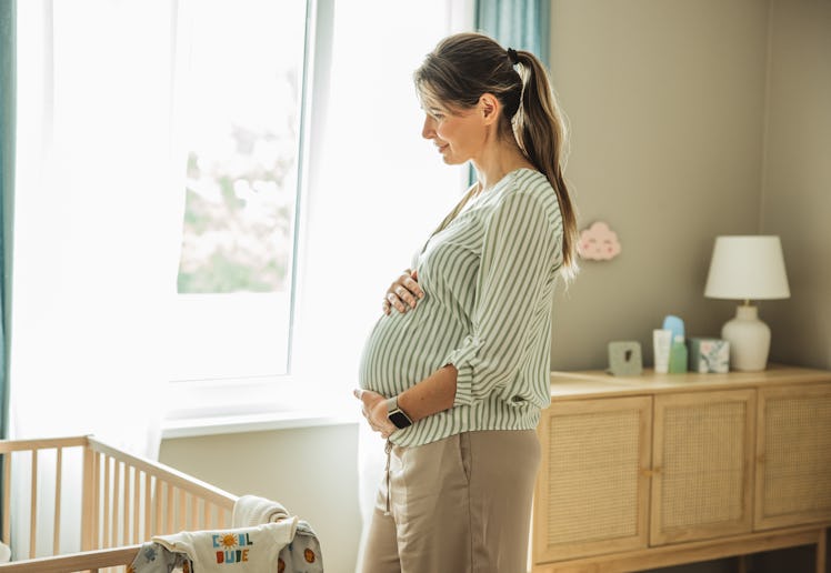 Pregnant woman standing next to crib and smiling.
