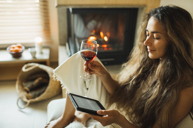 Leisure and relaxation in evening. Beautiful lady with long hair sitting on sofa at fireside and rea...