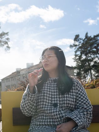 Woman smoking vape pen while sitting on bench at sunny day