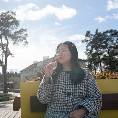 Woman smoking vape pen while sitting on bench at sunny day