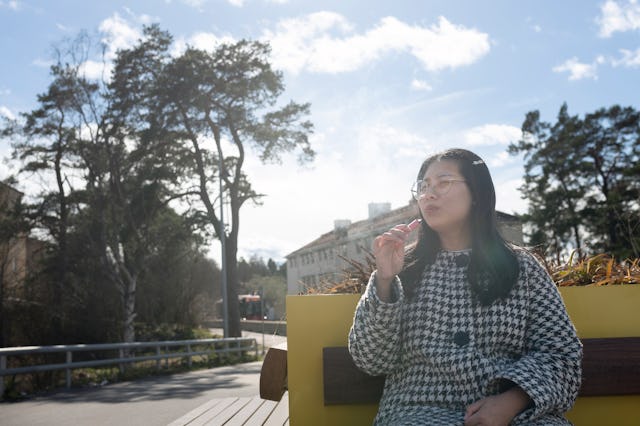 Woman smoking vape pen while sitting on bench at sunny day