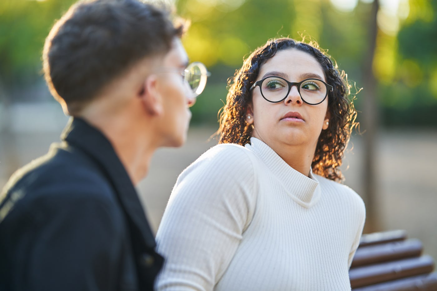 Young woman keeping distance and rejecting a man while having a date together outdoors in a park.