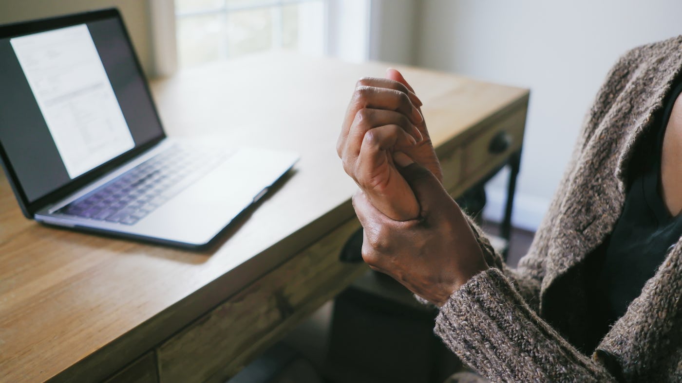 Close-up of unrecognizable black woman sitting at desk holding her hand in pain