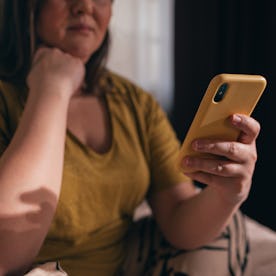 An unrecognizable plus size woman in a yellow T-shirt watching reels on her mobile phone.