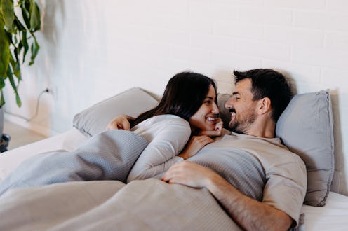 Young couple lying in bed, gazing into each other's eyes, sharing smiles and laughter, enjoying a co...