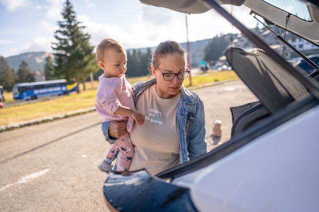 Mother with her baby girl behind the car preparing the trip