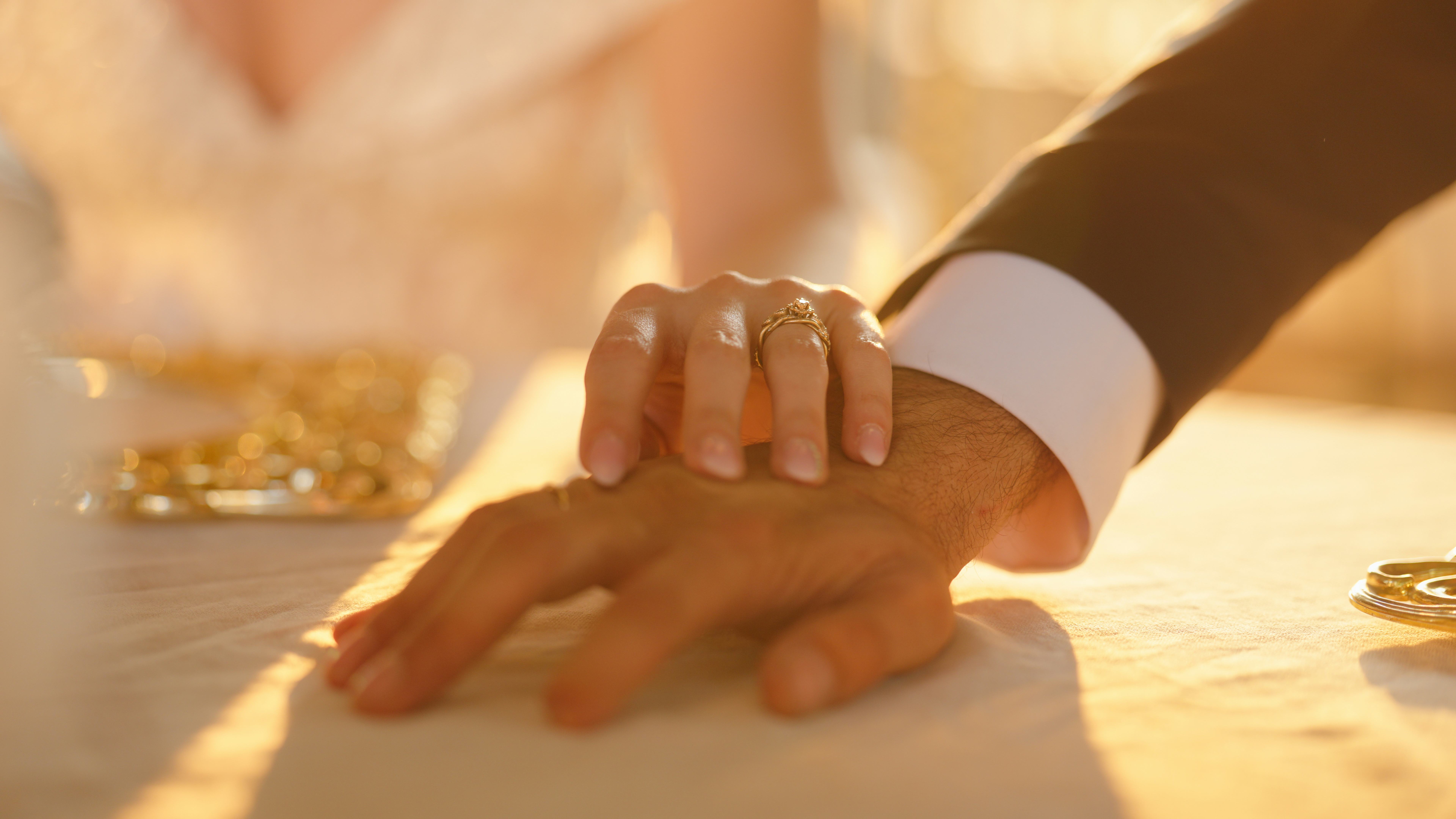 A close-up video of newlywed, young bride and groom, holding each other's hands. The wedding ring is...